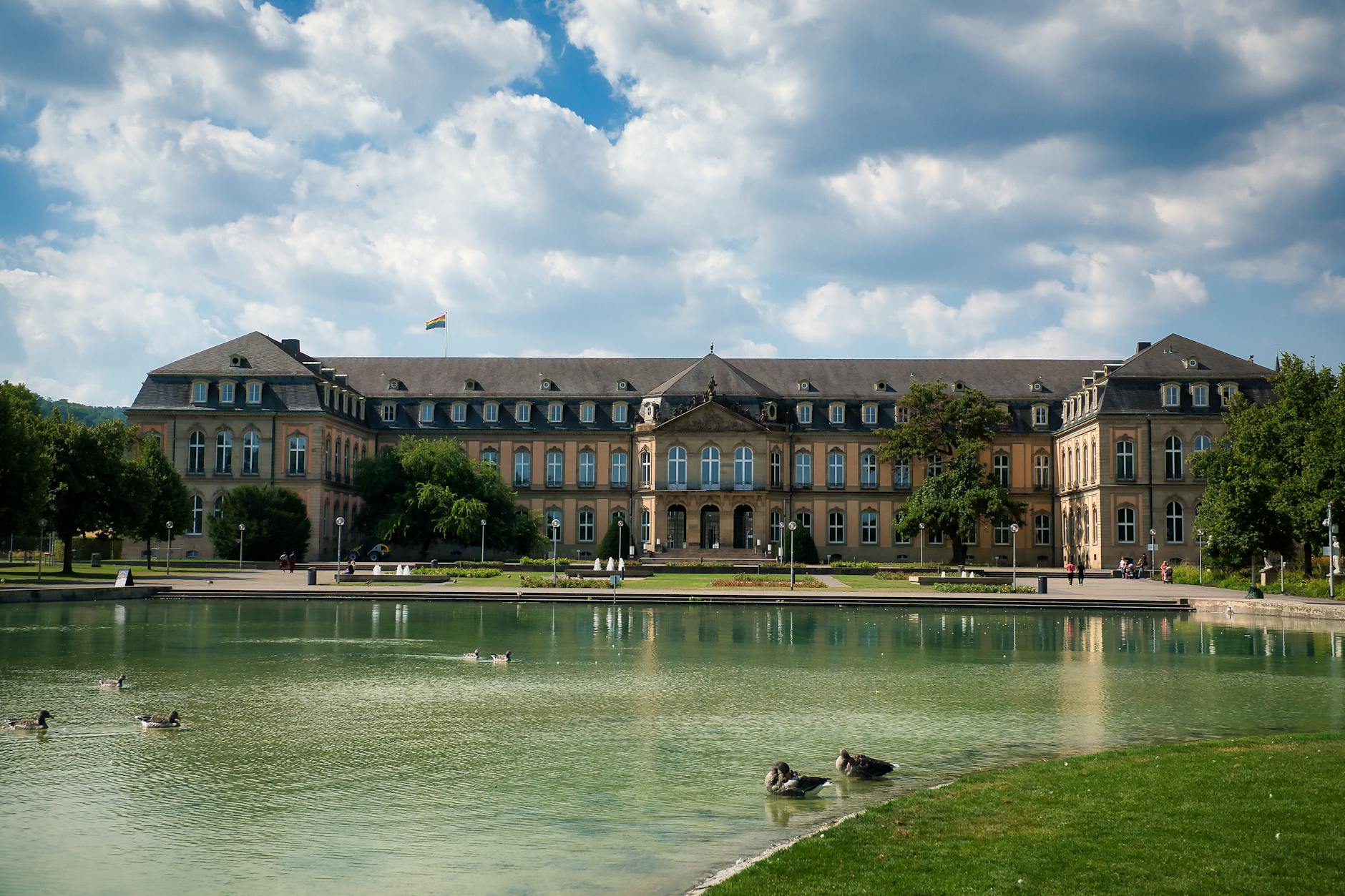 The Neue Schloss in Stuttgart captured on a sunny day with serene ducks by the pond, showcasing urban elegance.
