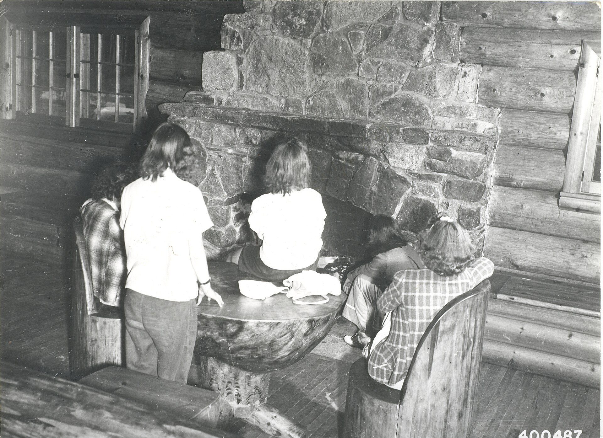 A group of young ladies warming themselves before the fireplace in the Community Building at the South Kawishiwi River Camp and Picnic Gr…